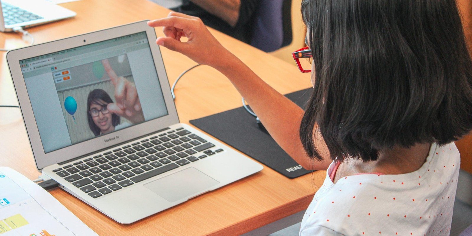 Photo of young person controlling a game via physical gestures in front of her laptop webcam